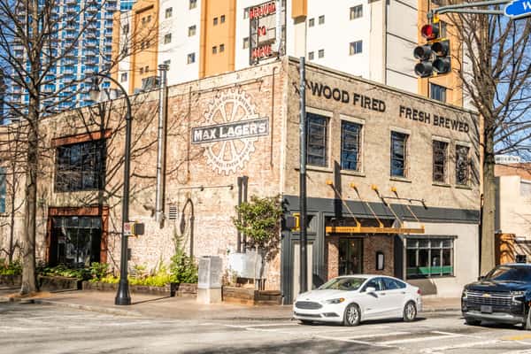 Corner view of Max Lager's American Grill & Brewery with signage reading "Wood Fired" and "Fresh Brewed," located at 320 Peachtree Street in Atlanta. A historic brick building surrounded by downtown city life.