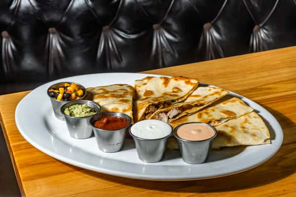 Grilled chicken quesadilla slices served with five dipping sauces including guacamole, salsa, sour cream, chipotle mayo, and black bean corn salsa. A Tex-Mex inspired appetizer perfect for sharing at a modern American eatery.