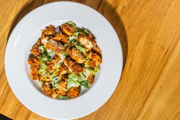 Top-down view of fried chicken pieces served over crisp romaine lettuce and creamy dressing. A crunchy, savory salad option perfect for a satisfying meal.