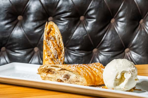 Flaky apple strudel drizzled with caramel and powdered sugar, served with a scoop of vanilla ice cream. A warm and comforting dessert perfect for pairing with a house-made brew.