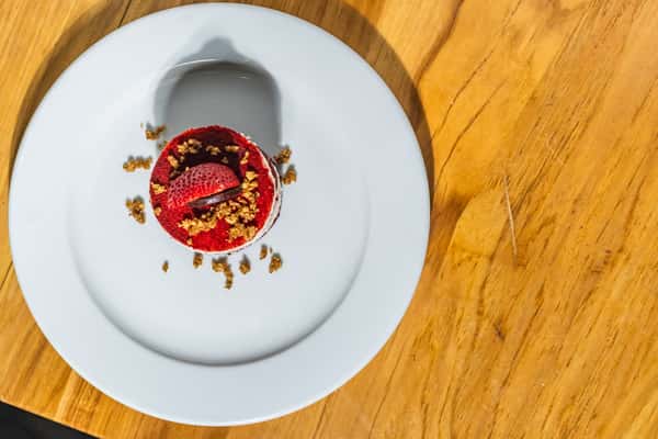 Top-down view of a mini red velvet cake topped with a sliced strawberry and sprinkled with crumble. A vibrant, indulgent dessert perfect for sharing or ending a meal.