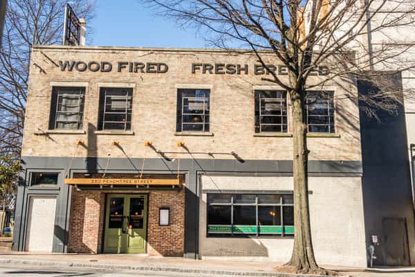 Street-level view of Max Lager's American Grill & Brewery at 320 Peachtree Street, showcasing its historic brick façade with bold signage: "Wood Fired" and "Fresh Brewed." A downtown Atlanta dining destination known for craft beer and wood-fired cuisine.