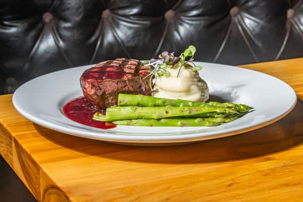 Grilled filet mignon with a red wine reduction, served with mashed potatoes and grilled asparagus, garnished with fresh microgreens. A refined steak entrée with rich, elegant presentation.