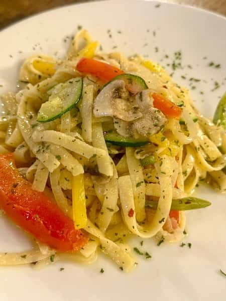 Vegetable fettuccine pasta tossed with sautéed zucchini, mushrooms, and bell peppers in a light garlic herb sauce, plated at an Italian-inspired restaurant.