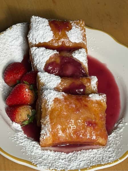 Golden, flaky strawberry cream cheese pastries dusted with powdered sugar, served with fresh strawberries and sweet strawberry sauce on a white dessert plate.