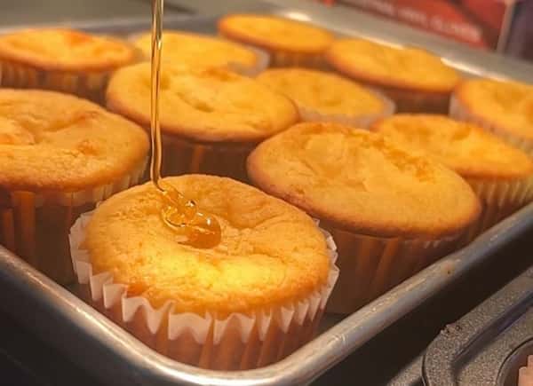 Freshly baked cornbread muffins in a metal tray, topped with a drizzle of golden honey for a warm Southern comfort food touch.