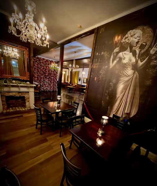 Elegant restaurant dining room with crystal chandeliers, dark wood tables, vintage fireplace, and a large mural of a classic jazz singer, creating a romantic upscale ambiance.