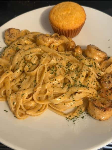 Creamy Cajun chicken fettuccine Alfredo with sautéed mushrooms, served with a cornbread muffin on a white plate.