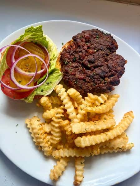 Classic hamburger steak patty with crinkle-cut fries, served with lettuce, tomato, pickles, and red onion on a white plate.