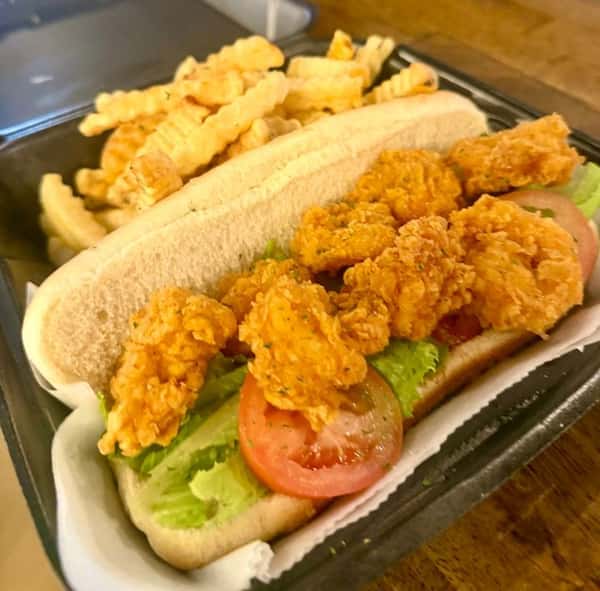 Crispy fried shrimp po' boy sandwich topped with fresh lettuce and tomato on a soft hoagie roll, served with golden crinkle-cut fries