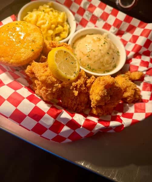 Crispy fried catfish fillets served with macaroni and cheese, mashed potatoes, cornbread, and a lemon wedge in a red checkered basket.