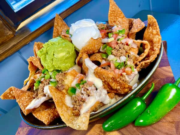 Loaded nachos with guacamole and toppings, with whole jalapeños on the side