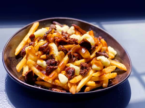 Bowl of loaded fries topped with sauce and chopped toppings