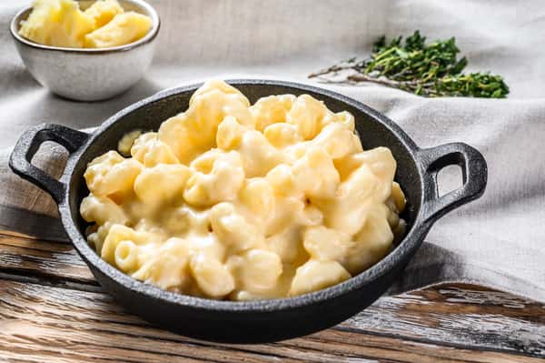 Skillet of creamy macaroni and cheese on a table with herbs nearby