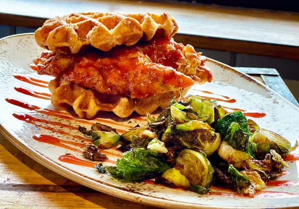 Chicken and waffles topped with sauce, served with Brussels sprouts on the side