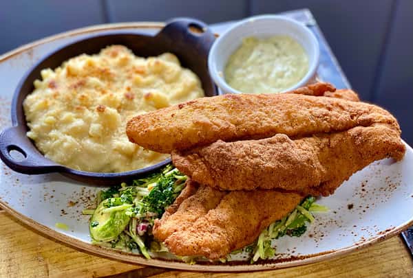 Fried fish fillets served with macaroni and cheese, greens, and a small cup of sauce on the side