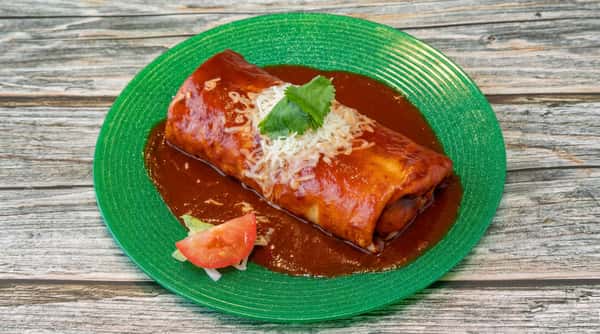 Burrito covered in red sauce, topped with shredded white cheese and cilantro, served on a green plate with lettuce and tomato.