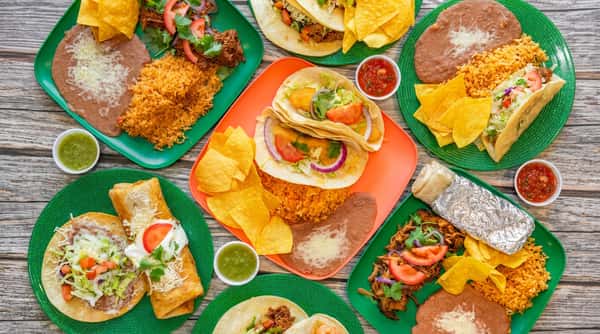 Assortment of Mexican dishes: tacos, burritos, flautas, rice, refried beans, chips, and salsa on colorful plates.