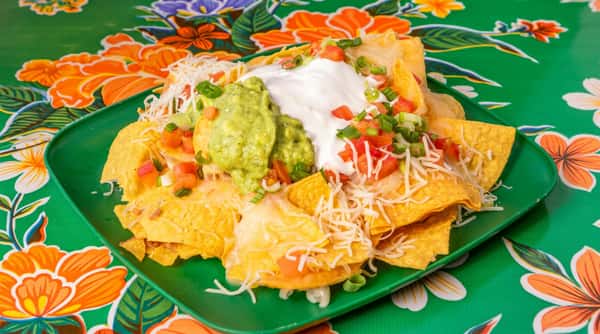 Nachos with melted cheese, guacamole, sour cream, diced tomatoes, and green onions on a green plate.