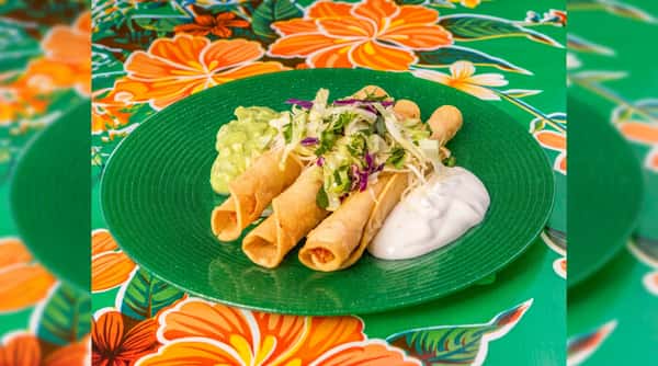 Golden brown taquitos topped with shredded lettuce, served with guacamole and sour cream on a green plate.