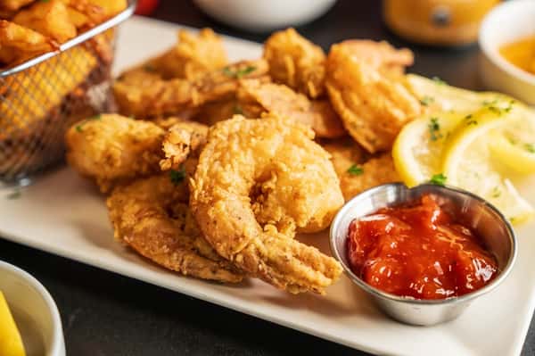 Golden fried shrimp with crispy breading served with cocktail sauce, lemon wedges, and fries on a seafood restaurant platter.