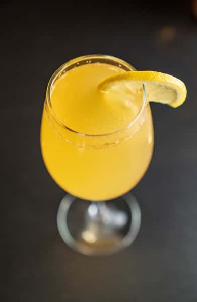 Chilled citrus cocktail garnished with a lemon wedge served in a stemmed glass on a dark bar table.