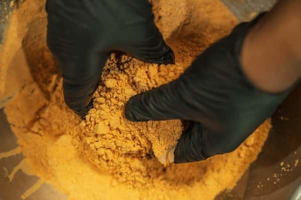 Chef wearing black gloves breading seasoned chicken in flour mixture during preparation for crispy fried chicken.