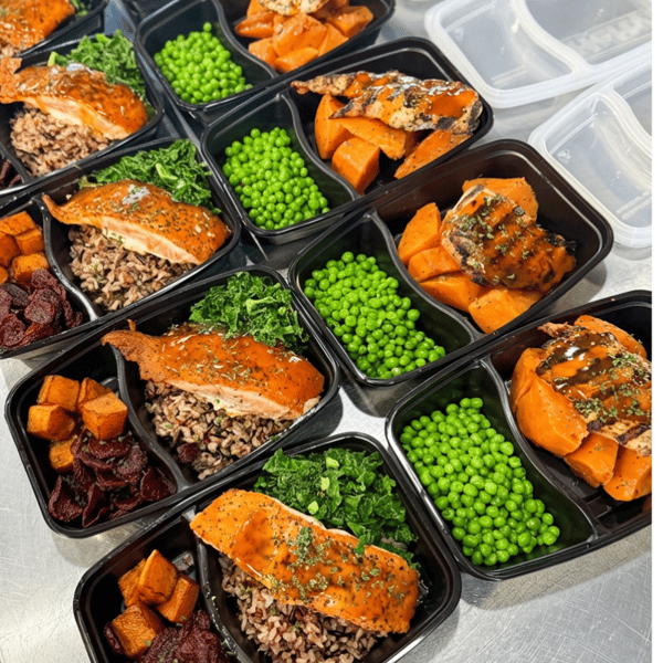 Close-up of gourmet salmon meal prep bowls with grains, roasted vegetables, kale, and green peas prepared in portioned containers for healthy meal prep service.