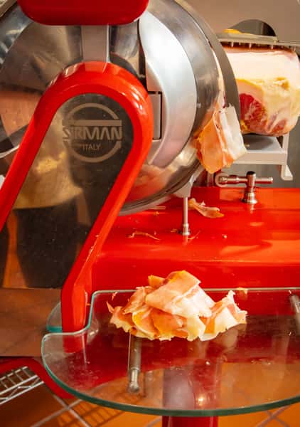 Freshly sliced prosciutto from a traditional Italian meat slicer at Dulivia Ristorante Italiano in Springdale, Utah, showcasing authentic Italian ingredients.