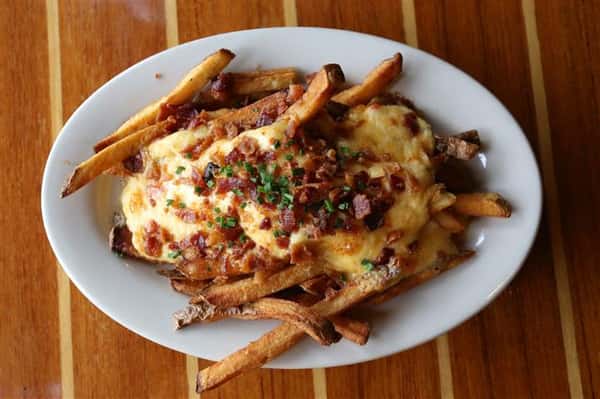 french fries on a plate covered in cheese, bacon and scallions.