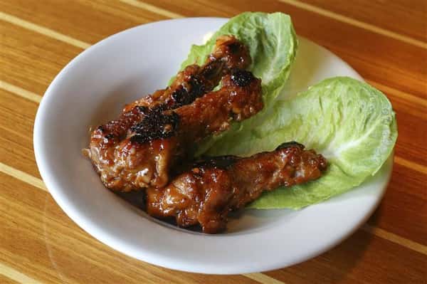 Three drumstick wings in a dark sauce on two romaine lettuce leaves