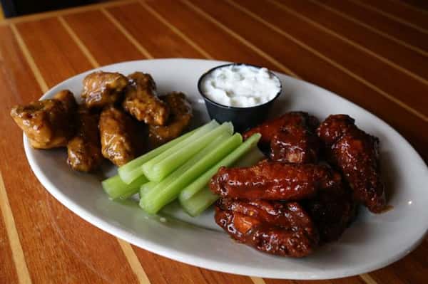 White plate with two different flavors of wings, celery and a side of bleu cheese.
