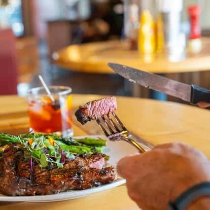 Steak garnished with greens, served with a fork and a drink