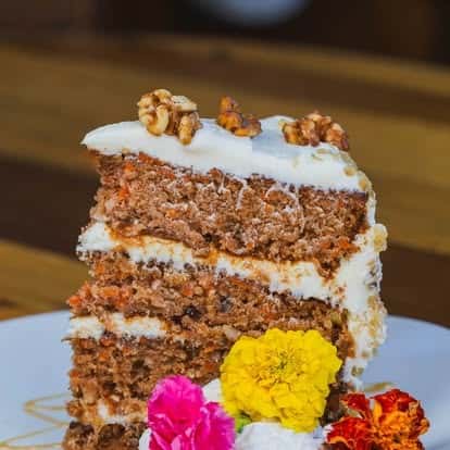 Layered carrot cake with cream cheese frosting, walnuts, and an edible flower garnish
