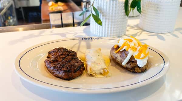 Steak dinner with a baked potato topped with cheese and sour cream and a side of creamy pasta.