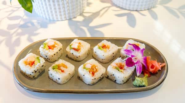 Shrimp and avocado sushi rolls with black sesame seeds, garnished with purple orchid, ginger, and wasabi.