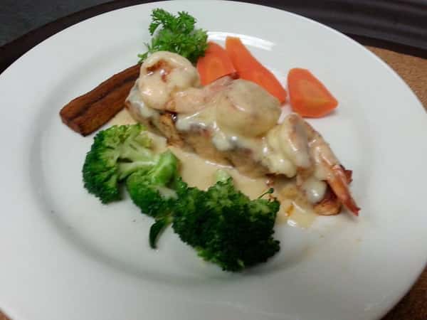 Salmon on a white plate with shrimp on top in a sauce