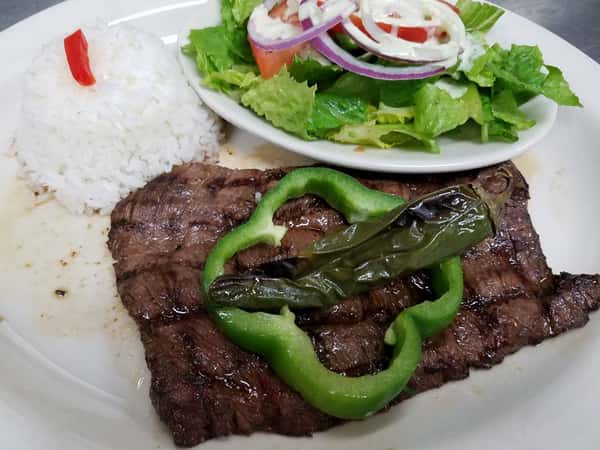 Steak on white plate with slice of bell pepper with roasted finger pepper on top