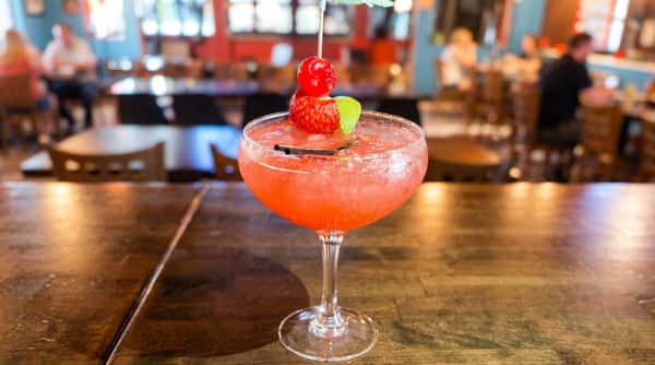 Strawberry cocktail in a coupe glass with a cherry, strawberry, lime, and paper umbrella.