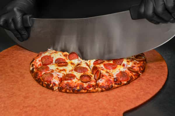 Chef cutting a pepperoni pizza with a large blade