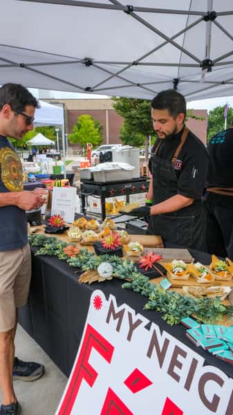 Chef serving signature bites at an outdoor food festival booth, highlighting local cuisine and community dining experiences.