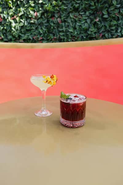 Two handcrafted cocktails served on a stylish outdoor patio table, featuring elegant presentation and a vibrant rooftop lounge atmosphere.
