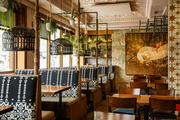 Stylish restaurant dining room featuring patterned booth seating, hanging greenery, natural light, and contemporary upscale décor.