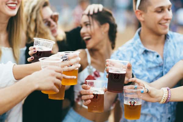 Friends raising craft beers in a celebratory toast at an outdoor social event, capturing a lively atmosphere, local brews, and community gathering.