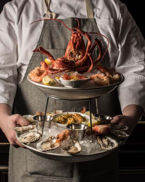 Luxury seafood tower featuring lobster, oysters, shrimp, and chilled shellfish, elegantly presented by a chef for an upscale dining experience.