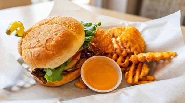 A double-patty hamburger with cheese, bacon, and pineapple, served with waffle fries on a white paper.