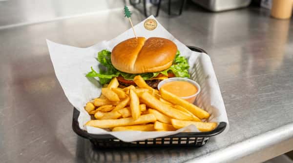 Burger with lettuce, tomato, and cheese; a pile of fries; and a cup of orange sauce, in a black basket.
