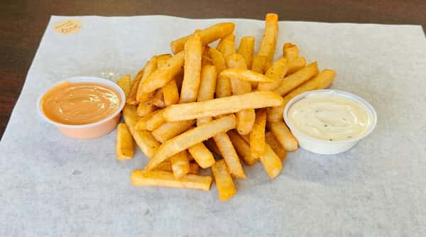 Golden french fries with two dipping sauces – one orange, one white – on white paper.