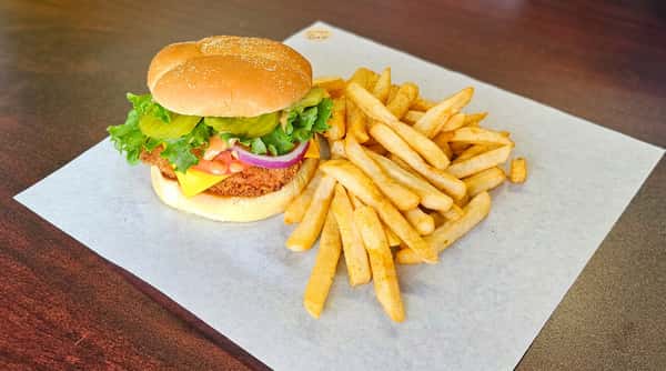 Crispy chicken sandwich with lettuce, pickles, red onion, cheese, sauce, and a side of french fries on parchment paper.