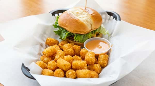 A basket with a burger, a side of tater tots, and a dipping sauce.